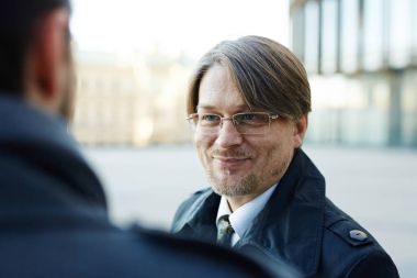 Baş ve omuzlar meslektaşı animatedly ofis binası, omuz görünümü üzerinde dururken sohbet neşeli orta yaşlı işadamı portresi