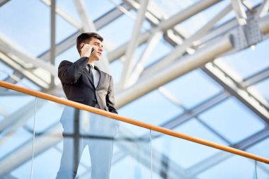Düşük açılı cam balkon modern ofis binası smartphone durarak konuşmak güçlü genç işadamı portresi