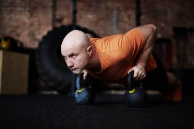 Tahta konumunu kettlebells yardımıyla ayakta ve uzak konsantrasyon ile tam uzunlukta portre seyir kel sportif adam