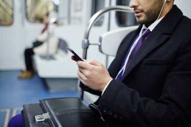 Smartphone kullanarak ve kulaklık müzik metro tren oturan genç Orta Doğu işadamı görüntüsünü yan görünümü