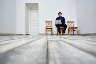 Office kapının yanında sandalyede bekleme odasında otururken dizüstü bilgisayar kullanan sakallı adam portresi düşük açılı