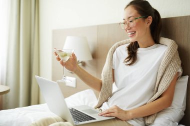 Güzel Asyalı kadın laptop gelen film izlemek ve hafta sonu martini içme rahat yatakta rahatlatıcı portresi