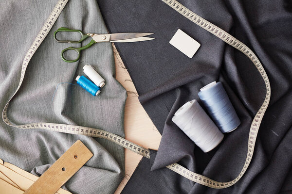 Background image of sewing items on grey fabric: scissors, measuring tape and thread