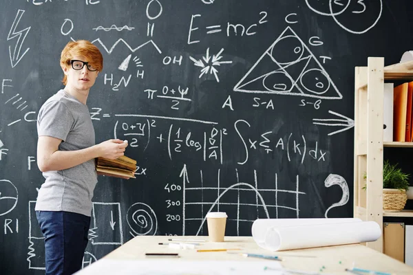 Portrait of young red haired student working at big blackboard writing science formulas in college class