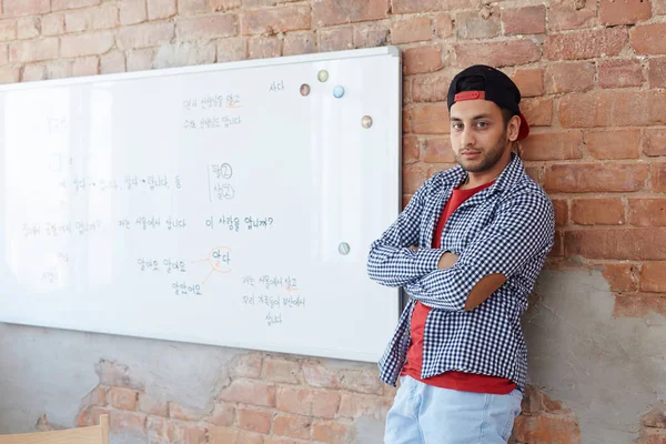 Serious student standing by wall and whiteboard