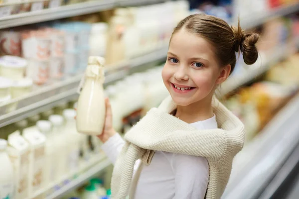 カメラ目線とスーパー マーケットの酪農場の通路で牛乳瓶を押しながら笑顔のかわいい少女の肖像画 — ストック写真