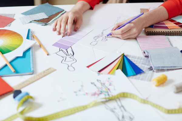 Женщина рисует новую модель платья сиреневым карандашом
