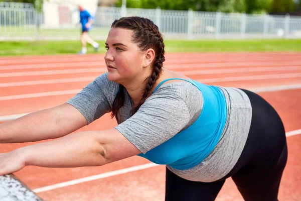 胖乎乎的女子在体育场上运动时伸展双臂 — 图库照片