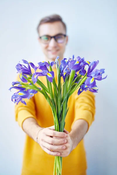 美しいアイリス焦点カメラに花の花束を渡す笑顔の若い男性の肖像画 — ストック写真