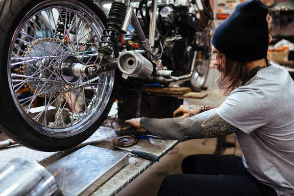 Wytatuowany motocykla mechanik mocowania w warsztacie — Zdjęcie stockowe