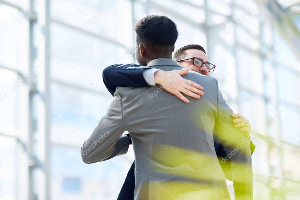 Portrait of two business partners hugging  and smiling with happiness standing in modern glass hall of office building