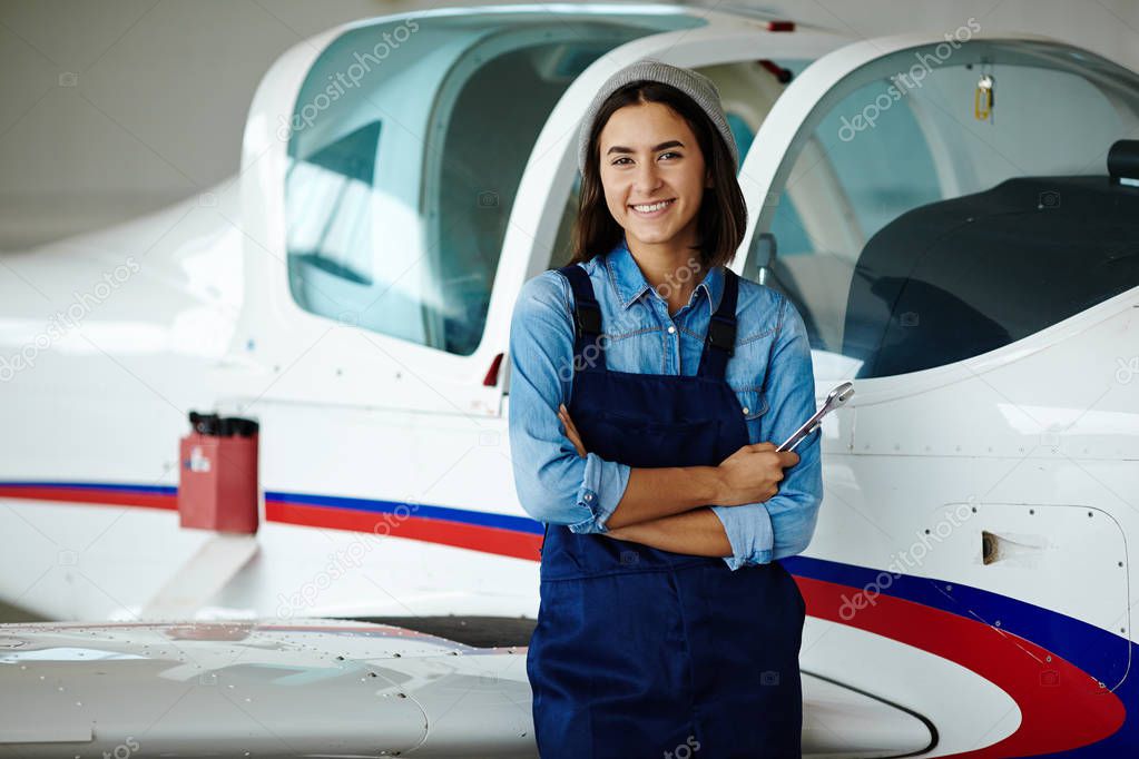 Portrait of modern young woman working in engineering standing by jet plane smiling and holding wrenches looking at camera