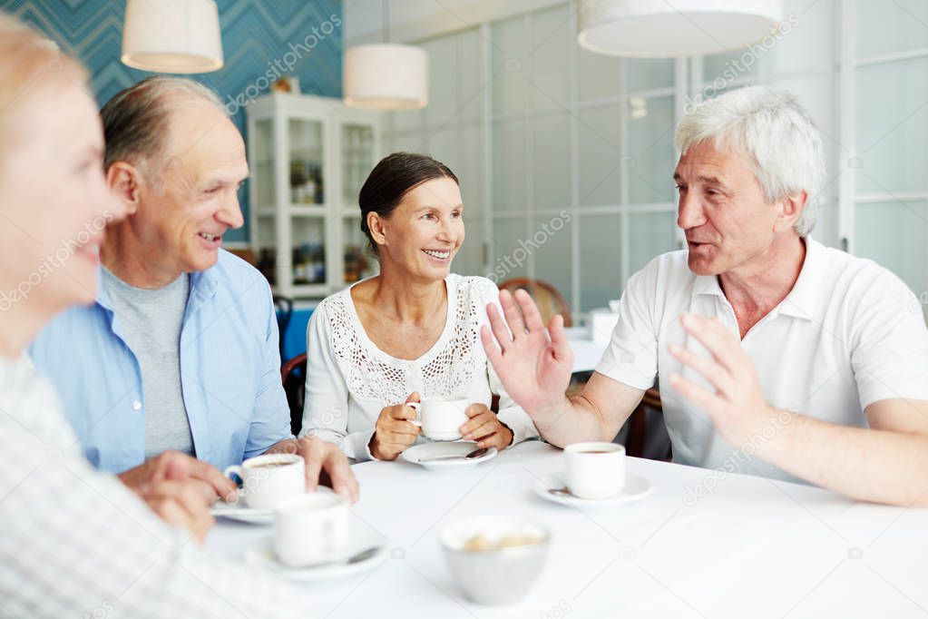 Group of friendly senior people gathered in cafe for talk by cup of coffee