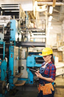 Çekici genç kalite kontrol Denetçisi'nde modern bitki üretim bölümünde dijital tablet kullanarak işçisi ve koruyucu gözlük