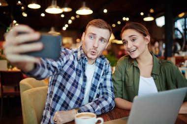 Güzel kahvehane iyi vakit geçiriyor: yüz buruşturma gülümseyen güzel arkadaşı ile dikey, bel selfie çekerken gösterilen yakışıklı genç