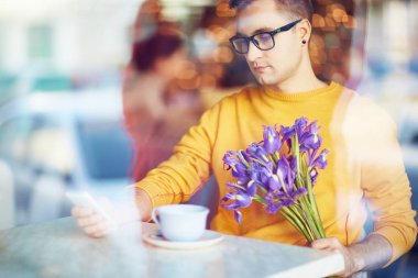 Süre servis için kız arkadaşı buket çiçek ile kafede masada telefon kullanan genç adam portresi