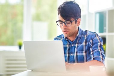 Çalışkan genç gazeteci ekose desenli gömlek arka plan üzerinde panoramik pencerelere ofis masa başında otururken dizüstü bilgisayarda yazı yazma