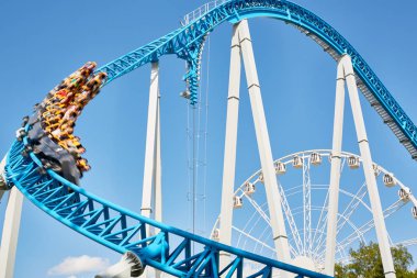 Açık mavi gökyüzü karşı bulanık çekimde hızlı aşağıya arabası ile uzun boylu roller coaster binmek