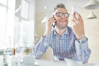 İki akıllı kullanarak neşeli orta yaşlı işadamı: o telefonda konuşurken ve ikinci telefonda sms okuma