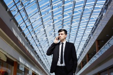 Telefon uzaklıkta modern ofis binası cam tavan altında bakarak konuşan başarılı emin işadamı portresi