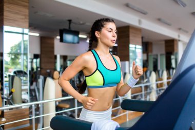 Renkli üst ve ferah modern salonunda treadmill kardiyo egzersiz yaparak tayt giyen sportif genç kadın portresi