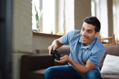 Video oyun holding kablosuz denetleyicisi oynama ve evde kanepede otururken sevinçle gülümseyen yakışıklı duygusal yetişkin adam portresi