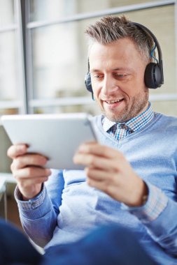 Meraklı orta yaşlı işadamı Kulaklığımda tablete online seminer izlemek için Internet kullanımı