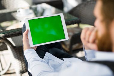 Dalgın Kızıl saçlı Yöneticisi omuz görünümü üzerinde açık kafe kamışı mobilya, baharda tadını çıkarırken bir konsantrasyon ile dokunmatik ekran arıyorum