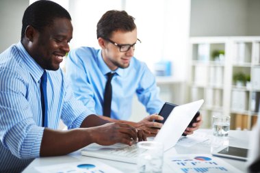 Verimli çalışma sürecinde geniş office: laptop meslektaşı dijital tablet üzerinde çalışan gözlük içinde iken metin yazarak dişlek gülümseme ile orta yaşlı çalışan