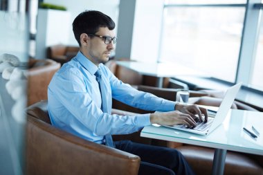Panoramik pencereli ferah ofis lobisinde otururken dizüstü üzerinden finans piyasası analiz yakışıklı sakallı tüccar