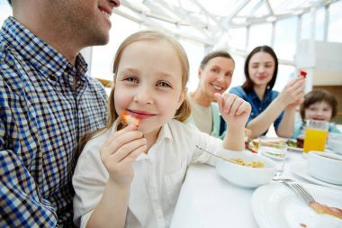Aile çevresi kahvaltı yemek yerken kameraya bakarak mutlu çocuk
