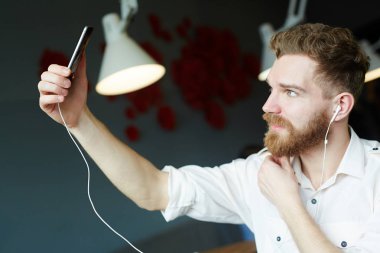Yan görünümü selfie fotoğraf için poz smartphone kamera bakarak yakışıklı sakallı adam portresi