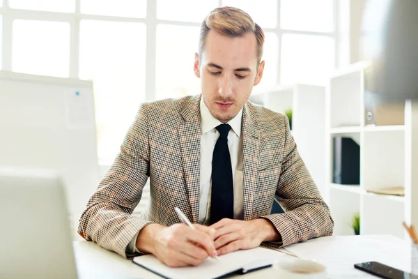 Young economist organizing his work or writing agenda in notebook