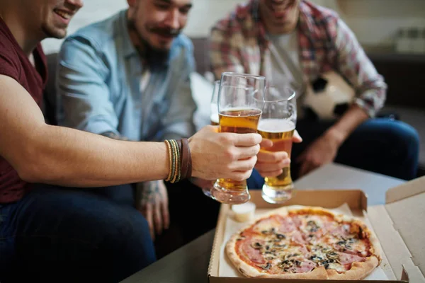 Closeup portrait of group of friends meeting at home toasting with beer and eating pizza while watching football match