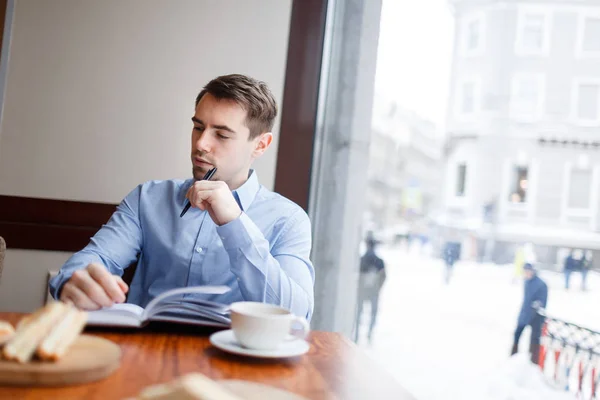 ペンとノート朝食後にカフェの窓際で座って物思いにふける男 — ストック写真