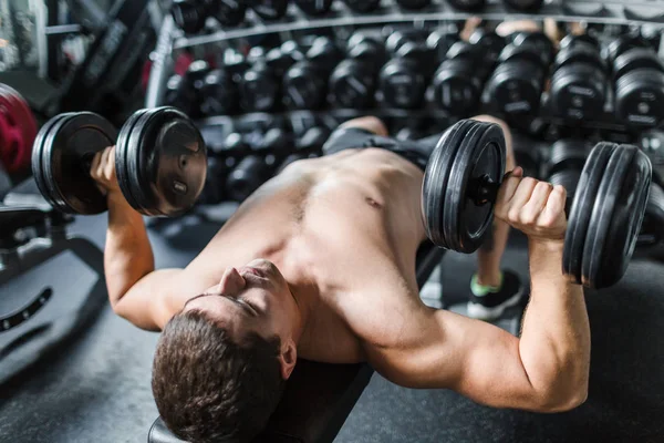 赤裸上身的肌肉人的画像在现代健身房的力量训练中做哑铃的工作 — 图库照片