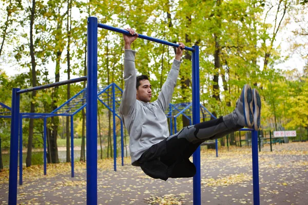 在秋季街健身公园的单杠上悬挂腿部升降机的英俊年轻运动员的肖像 — 图库照片
