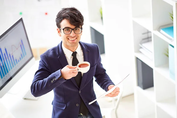 微笑的经理与一杯茶和文件站在办公室工作 — 图库照片