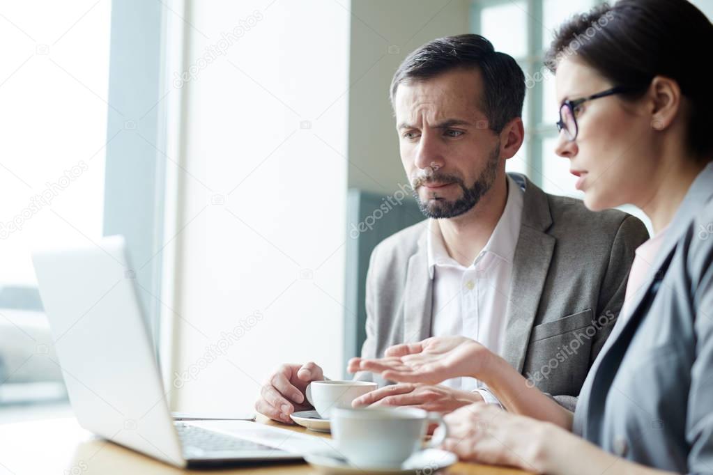Modern traders discussing online information by cup of coffee