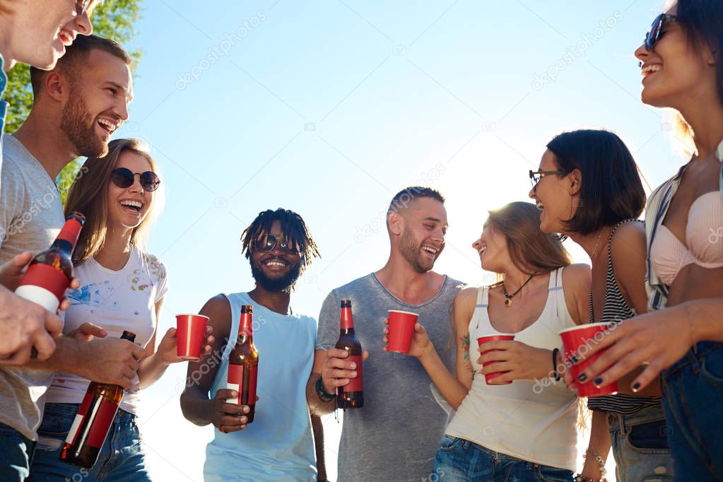 Joyful friends with beer talking at beach party