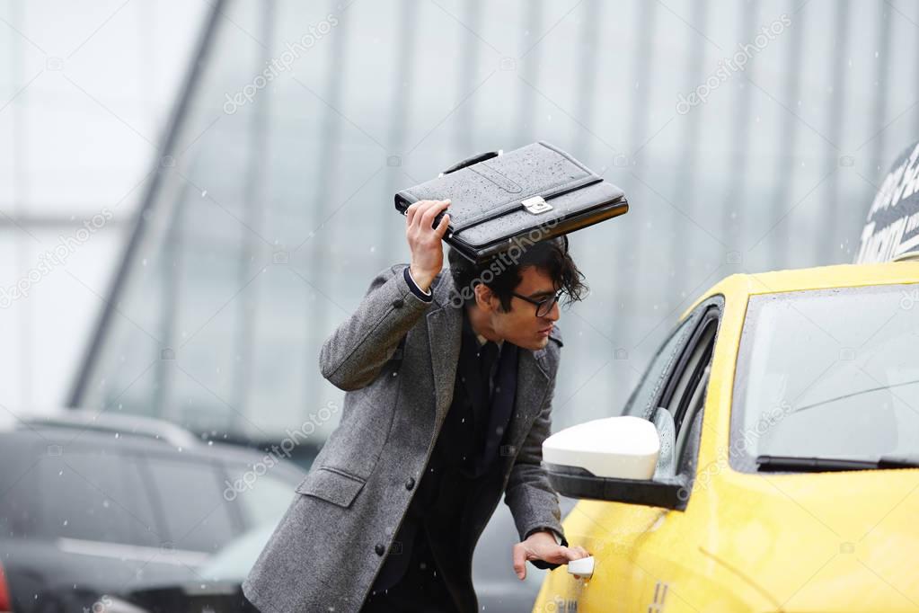 Portrait of disheveled Middle-Eastern businessman hurrying to catch taxi cab on rainy autumn street, covering head with briefcase
