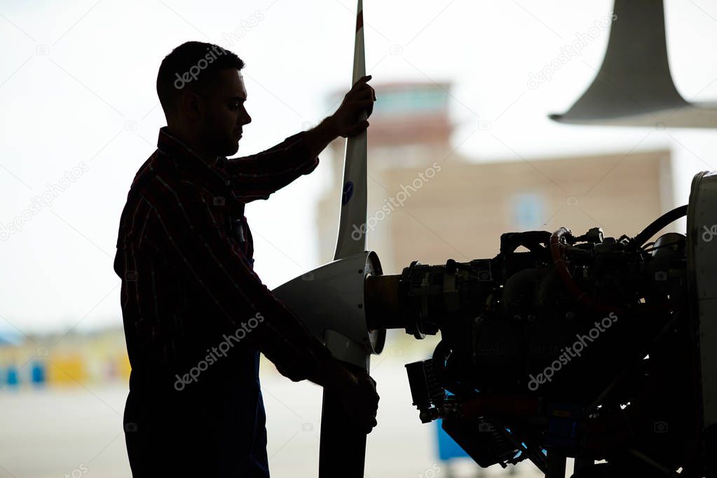 Dark silhouette of aircraft engineer dismantling jet plane in hangar, taking of propeller part and checking turbines
