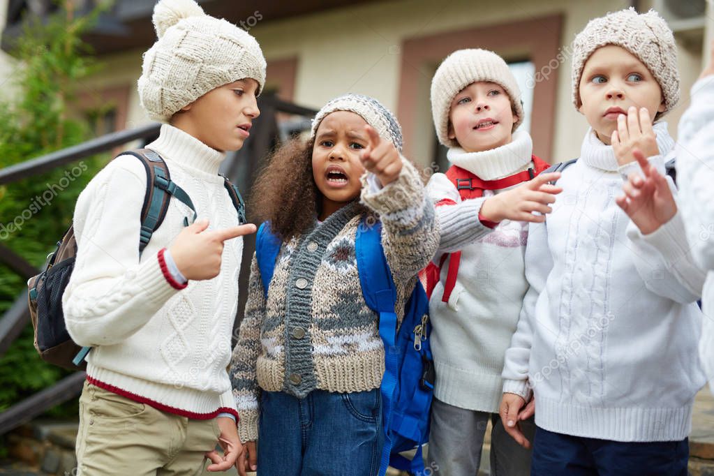 Group of little kids with rucksacks having talk after classes