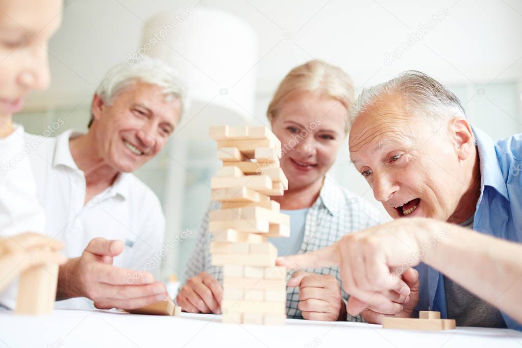 Group of old friends building structure from wooden blocks on table