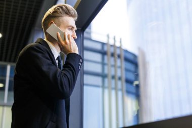 Bel öğe, dikey, yakışıklı girişimci onun arkadaşına Smartphone'da ofis lobisinde, profil görünümü kısa ara harcama süre söz