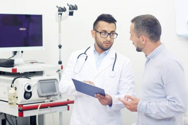 Erkek hasta ile tıbbi test sonuçlarını tartışıyor ve gerekli tedavi, iç arka plan üzerinde modern ofis reçete gözlük yakışıklı genç doktor