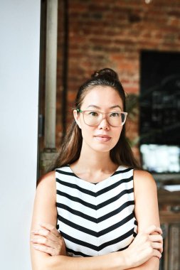 Çapraz kolları, arka plan üzerinde modern Studio iç olan fotoğraf için poz iken pretty Asya tasarımcı yaslanmış duvara