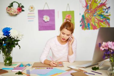 Kadın Illustrator smartphone cep telefonu ile onun arkadaşı ile küçük bir konuşma, ileti örneği ve defter ön plan üzerinde dağınık masa görürken ile pembe kalem eskiz yaparken konsantre