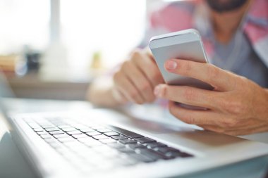 Tanınmayan adam manifatura iletinin smartphone cep telefonu ile yakın çekim ne zaman o masada dizüstü bilgisayar ile çalışma