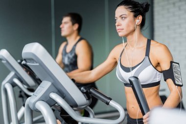 Eliptik makinesi kullanma ve modern spor olarak çalışma sırasında uygun adamın yanında müzik dinlerken egzersiz güzel sportif esmer kadın portresi